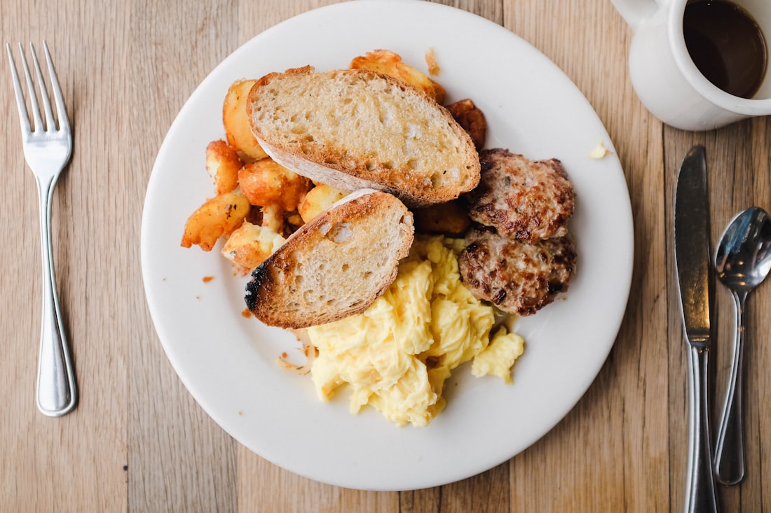 A hearty breakfast plate of eggs, sausage and toast with a cup of coffee on a wooden table