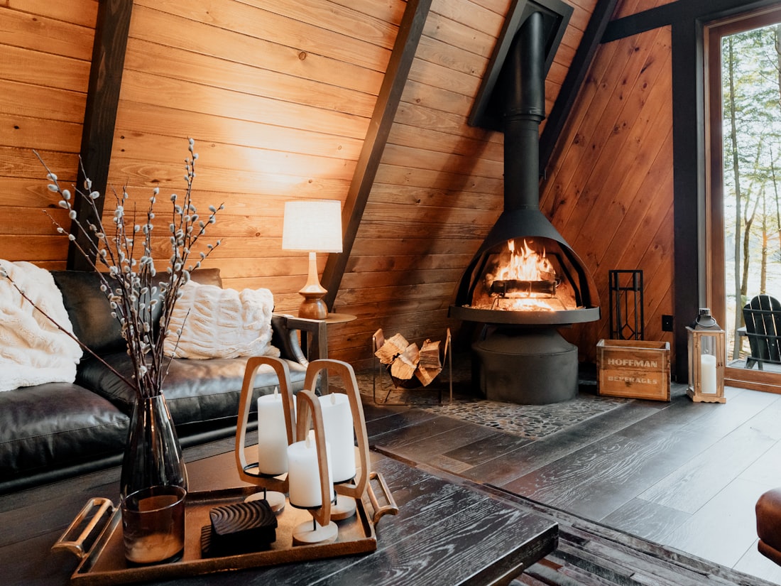 A warm log-house sitting room with a wood stove, soft lamplight and honey-toned timber walls
